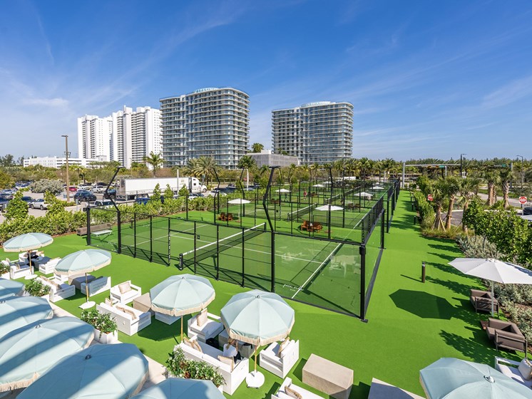 A tennis court surrounded by green grass and white umbrellas.